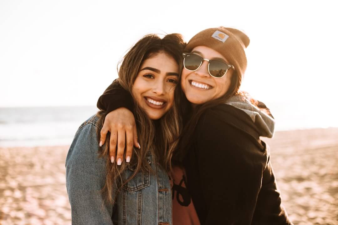 Photo by Omar Lopez woman hugging other woman while smiling at beach